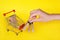 Mini cart and female hand with small craft bags on yellow background.