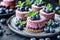 Mini cheesecake topped with fresh blueberries and mint leaves on black plate. Delicious no bake berry cheesecake.