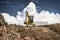 Mini excavator at the construction site on the edge of a pit against a cloudy blue sky. Compact construction equipment for