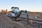 Mini excavator digg trench to lay cables concrete curbs and paving slabs at construction site. Backhoe on earthwork/roadworks