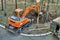 Mini excavator digging a trench among the trees for repairing city communications