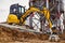 A mini excavator rams the ground with a vibrating plate. Laying of underground sewer pipes and communications during construction