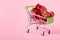 Mini green shop cart with small gift boxes on pink background, blank copy space, close up