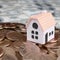 Mini house model on big coins stack on many dollar bills as background