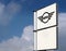 Mini logo in the dealership of the area, against blue sky with clouds. It is the symbol of the british car manufacturer.