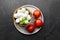 Mini mozzarella cheese balls in wooden bowl with red tomatoes on black stony background