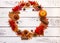 Mini orange pumpkin, dehydrated orange slices, red maple leaves, and arrow-wood berries form a wreath on a brown rustic wooden