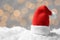Mini Santa hat on artificial snow against blurred Christmas lights