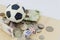 Mini soccer ball on top of playing cards with dices and money in different currency.