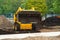 A mini tractor pours the soil out of the bucket, a yellow excavator is at work. Close-up