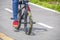 Mini trick stunt bike with camouflage fat tires and pegs being ridden by guy in red tennis shoes and blue jeans on paved surface