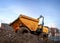 Mini yellow dumper with roll bar and orange flashing lights and tipper front bucket parked on construction soil rubble houses