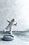 Miniature astronaut balancing on moon in spacesuit on gray textured background.