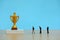 Miniature business concept - group of businessman lining up behind the golden trophy