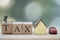 Miniature businessman standing on wood words TAX and miniature home and car