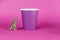 A miniature dinosaur and a paper cup against a purple background. A lilac disposable drink glass. Green figure of a predatory