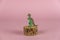Miniature dinosaur on a pedestal against a pink background. A small figurine of a predatory dinosaur on a round pine stand.