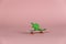 Miniature dinosaur riding a mini skateboard. Small green children`s toy against a pink background. Close-up.  Selective focus