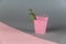 Miniature dinosaur sitting on a pink bucket.  Small green figurine of a predatory dinosaur. Metal bucket with handle. Gray-pink