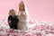 Miniature figures of spouses, bride and groom, standing in a mini-meringue pink and white on a pink background. Wedding miniature