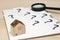 Miniature house and many question marks on white papers. House with question marks and magnifying glass. Real Estate Concept.