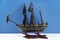 Miniature model of old ship with black sails on white table against blue background