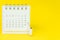 Miniature people figures using paint roller on white clean desktop calendar on solid yellow background with copy space, schedule