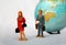 Miniature people and globe background. First mini lady figure and gentlemen behind her. Maybe marriage quarrel on the trip