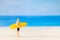 Miniature people man in a swimsuit, and holding a yellow surfboard on the beach