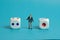 Miniature people toy figure photography. A shrugging businessman standing in the middle of white dice.  on blue background