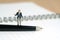 Miniature people toy figure photography. Signing agreement concept. A shrugging businessman stand above a black pen and opened