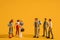 Miniature people on a yellow background, men against women at work. The concept of gender equality, feminism