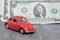 Miniature red car on the background of us dollars banknotes. Red retro toy car and money on gray background. Savings concept