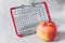 A miniature shopping basket and a red apple next to it