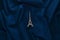A miniature statuette of the Eiffel Tower on a dark blue cloth background. Souvenir from Paris. Trend minimalism.
