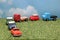Miniature toy cars on green grass over blue sky and clouds.