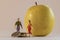 Miniature woman and man figure standing next to big yellow apple and counting coins. Shallow depth of field background. Family