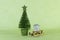 Miniature wooden sledge carrying a small gift next to a bright green Christmas tree on a light green background