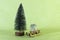 Miniature wooden sledge carrying a small gift next to a bright green Christmas tree on a light green background