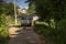 A minibus moving the dirt road near house, trees. A girl walkin from the beach