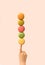 Minimal arrangement of child hand with finger index pointing up and holding stacking up macaroons. Pastel pink background