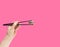Minimal asian artisan food concept. The man\'s hand holding black chopsticks with green yummy macaron. Bright pink background