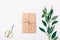 Minimal flat lay arrangement of fresh leaves and present wrapped in eco kraft paper. Gift box, scissors and green twig on white