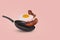 Minimal idea with a frying pan and a flying fried egg and bacon on a pastel pink background. Creative food concept
