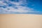 Minimal image of a landscape with two colors blue and yellow, desert ground or soft sandy beach and blue sky with white clouds.