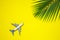 Minimal layout with model airplane and green tropical palm leaf on yellow background. Directly above. Travel vacation summer