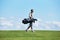 Minimal side view rich man carrying golf bag walking on green field against sky