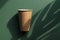 Minimal style composition made of eco friendly craft paper cup on green sunlit background with monstera leaf shadow. Recycling