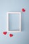 Minimal valentine day concept. White empty photo frame with hearts on blue background. Flat lay, top view, copy space .