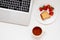 Minimal workspace: laptop with tea and breakfast, strawberries with cake. Flat lay perspective, top view